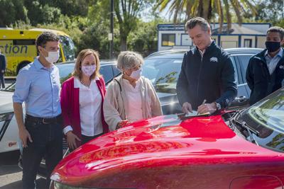 On the hood of an electric car, California Gov. Gavin Newsom signs an executive order requiring all new passenger vehicles sold in the state to be zero-emission by 2035 on Sept. 23, 2020, at Cal Expo in Sacramento.