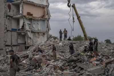 Rescue workers stand on the rubble at the scene, in the aftermath of a Russian rocket that hit an apartment residential block, in Chasiv Yar, Donetsk region, eastern Ukraine, Sunday, July 10, 2022.