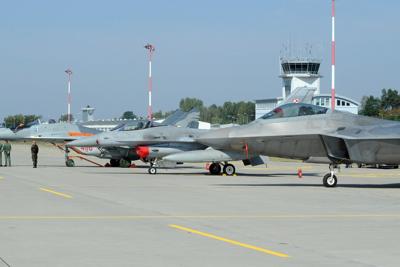Officials walk past fighter jets parked on the apron, a Polish Air Force Mig-29, left, Polish Air Force F-16, center and U.S. F-22 Raptor at a military base in Lask, Poland, on Aug. 31, 2015.