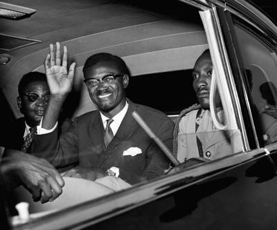 Congo Premier Patrice Lumumba waves as he sits in car for the drive from Idlewild Airport, New York, July 24, 1960 after his arrival from Europe. The Premier, 34, accompanied by nearly a dozen Congo officials, flew to New York to present the problem of ...