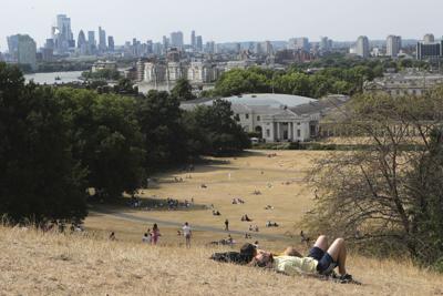 People sit on the sun-parched grass in Greenwich Park with the London skyline in the background  July 17, 2022.