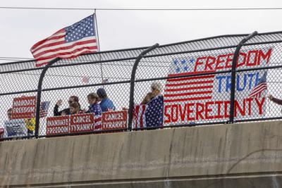People watch from an overpass as vehicles with the People Convoy of Truckers, protesting mandates and other issues, drive past on March 6, 2022, in Frederick, Md.